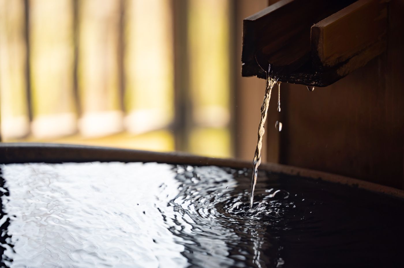 Water pouring from a wooden spout into a hinoki tub